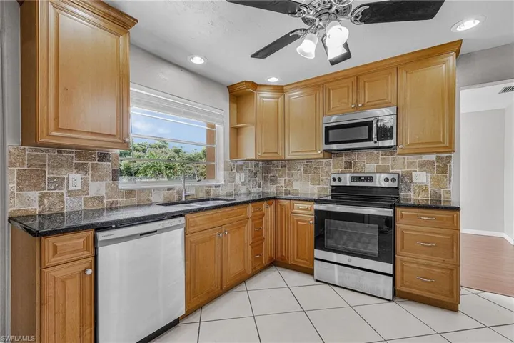 Kitchen with appliances with stainless steel finishes, light tile patterned floors, recessed lighting, tasteful backsplash, and dark stone countertops
