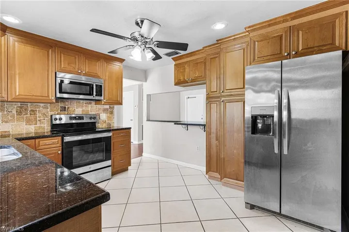 Kitchen featuring stainless steel appliances, dark stone counters, decorative backsplash, brown cabinets, and light tile patterned flooring