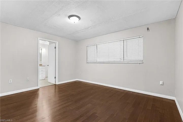 Unfurnished bedroom with dark wood-style flooring, a textured ceiling, and ensuite bath