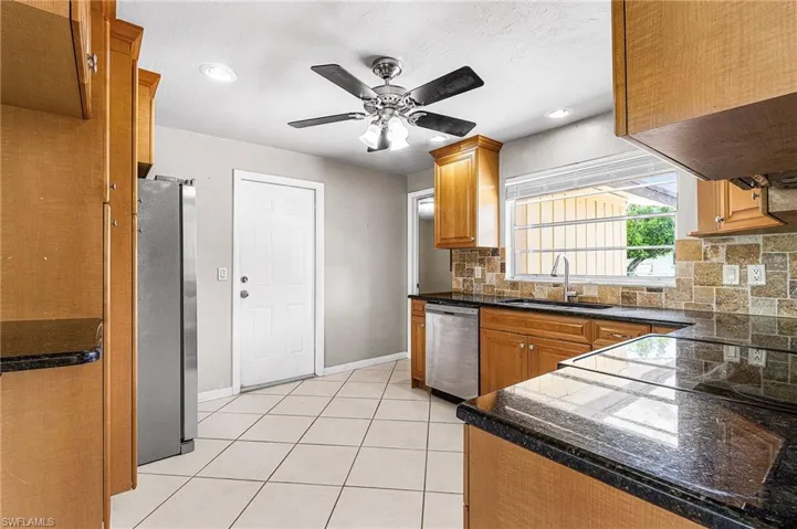 Kitchen with tasteful backsplash, light tile patterned flooring, appliances with stainless steel finishes, recessed lighting, and dark stone countertops