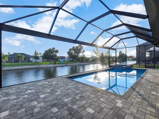 View of swimming pool featuring a water view, glass enclosure, a sunroom, a pool with connected hot tub, and a patio area