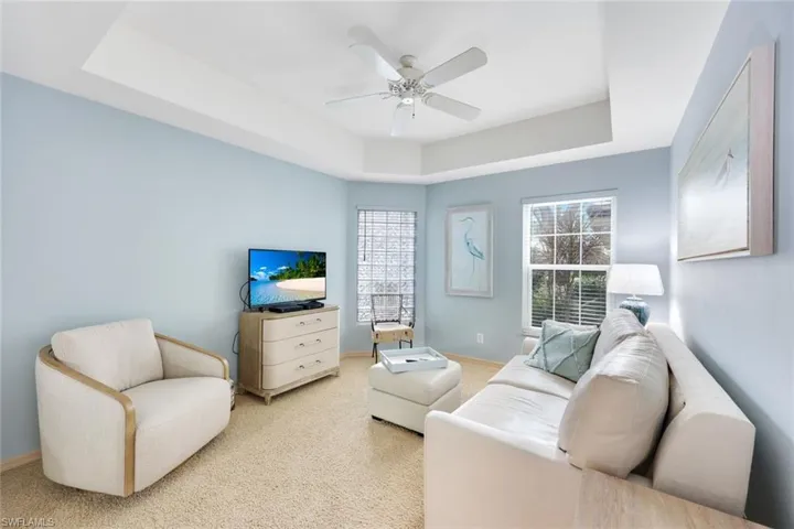 Carpeted living room featuring a tray ceiling and ceiling fan