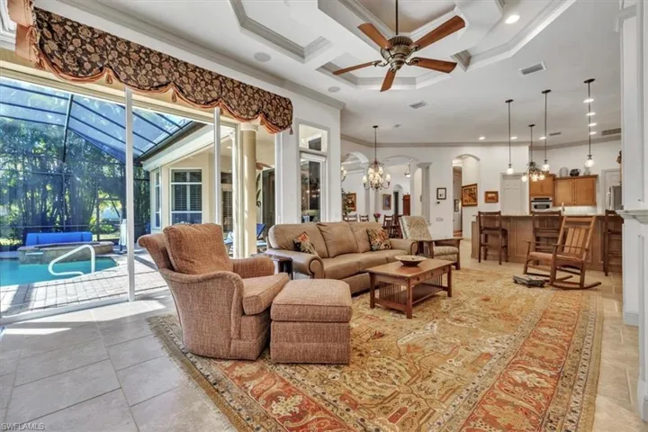 Living area featuring coffered ceiling, a sunroom, a ceiling fan, crown molding, and arched walkways