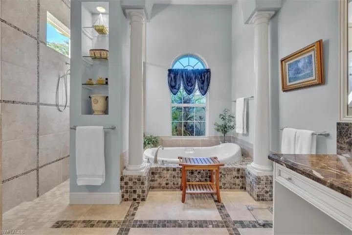 Full bath featuring decorative columns, a garden tub, a walk in shower, light tile patterned floors, and vanity