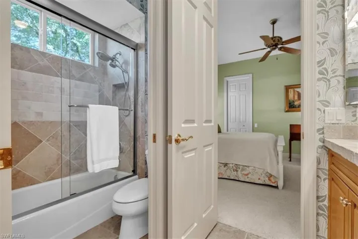 Full bathroom with vanity, enclosed tub / shower combo, connected bathroom, light colored carpet, and ceiling fan