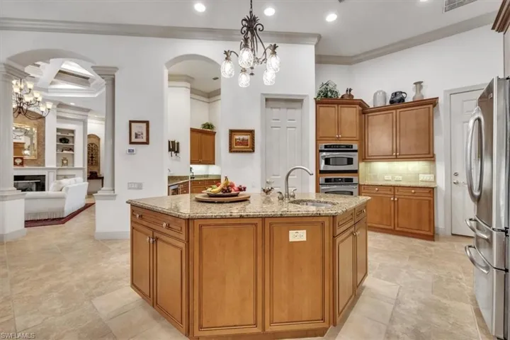 Kitchen with wood finish cabinets, arched walkways, hanging lights, light stone countertops, and ornamental molding