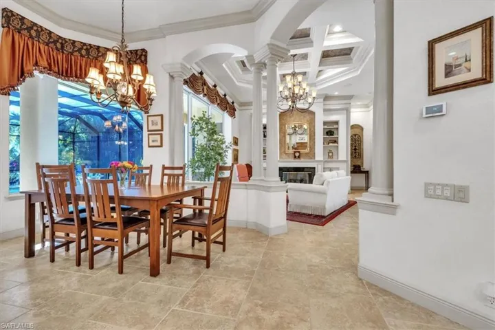 Dining space with coffered ceiling, hanging lights, crown molding, arched walkways, and a glass covered fireplace