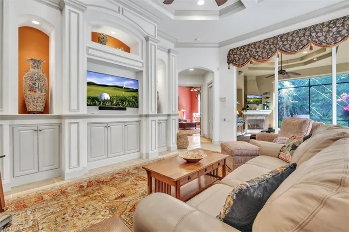 Living room with a ceiling fan, crown molding, arched walkways, and a fireplace