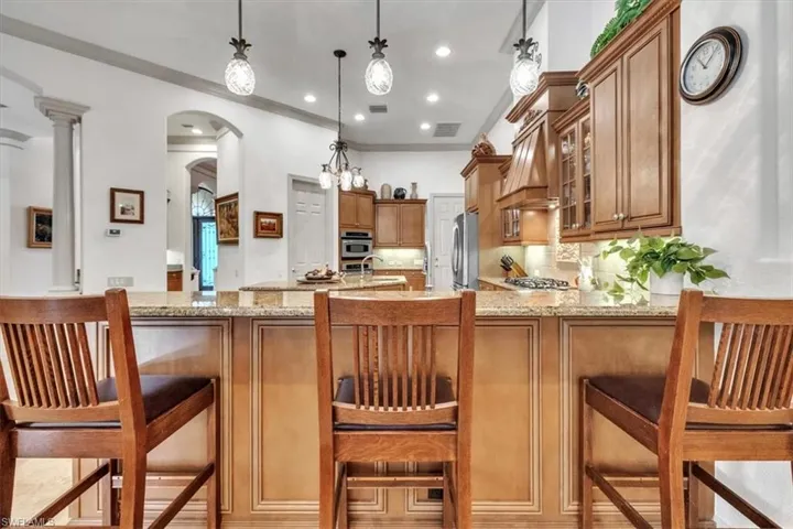 Kitchen featuring a breakfast bar area, wood finish cabinets, light stone counters, arched walkways, and crown molding