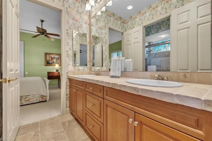 Ensuite bathroom with double vanity, light carpet, a shower with shower door, light stone finish floors, and wallpapered walls
