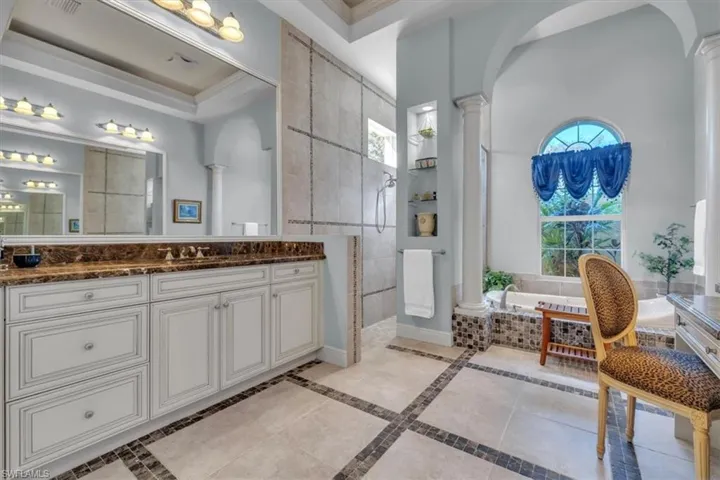Bathroom featuring decorative columns, a walk in shower, vanity, a garden tub, and ornamental molding