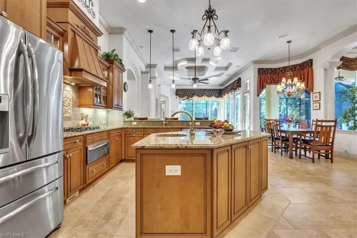 Kitchen featuring wood finish cabinetry, stainless steel fridge with ice dispenser, crown molding, ceiling fan, and light stone counters