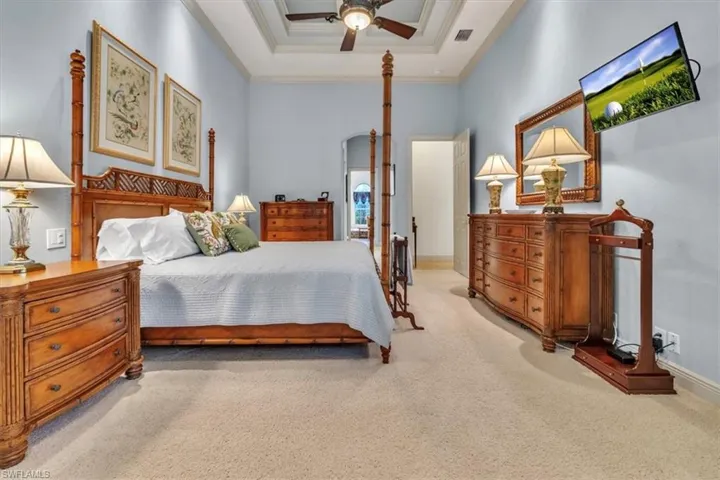 Bedroom featuring light carpet, a ceiling fan, a raised ceiling, and crown molding