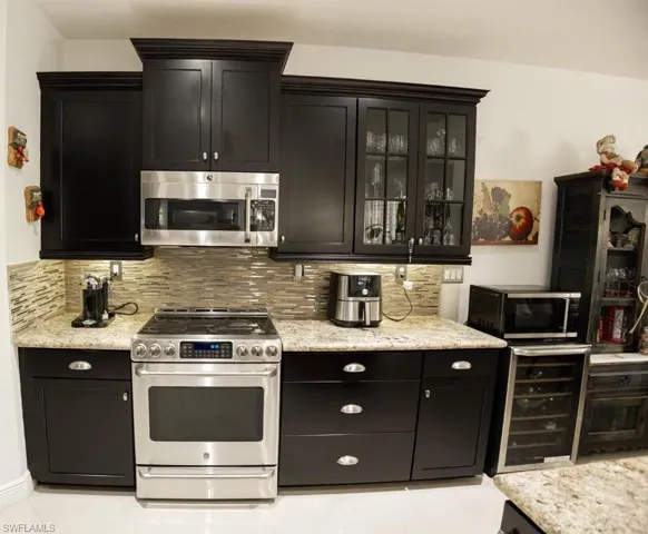 Kitchen featuring dark cabinetry, appliances with stainless steel finishes, backsplash, and light stone counters