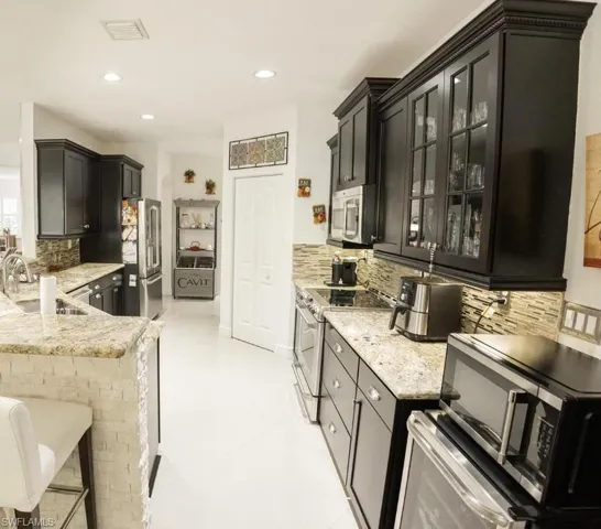 Kitchen with appliances with stainless steel finishes, tasteful backsplash, light stone counters, dark cabinetry, and recessed lighting
