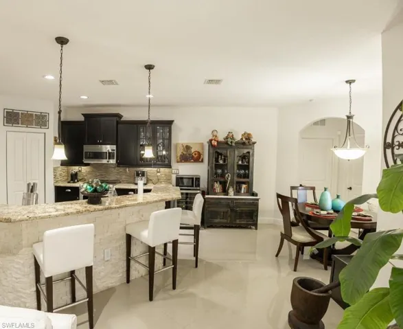 Kitchen featuring a kitchen breakfast bar, pendant lighting, backsplash, light stone countertops, and glass insert cabinets