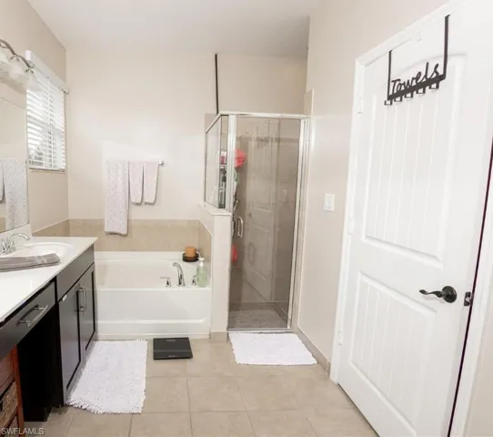 Full bathroom featuring a bath, light tile patterned flooring, vanity, and a shower stall