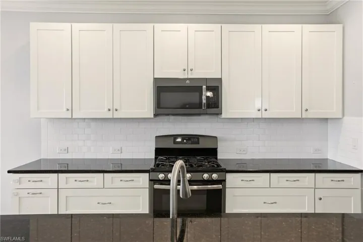 Kitchen featuring gas range oven, stainless steel microwave, white cabinetry, and dark stone counters