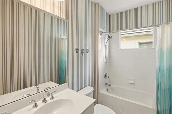 Bathroom featuring wallpapered walls, shower / tub combo, and vanity