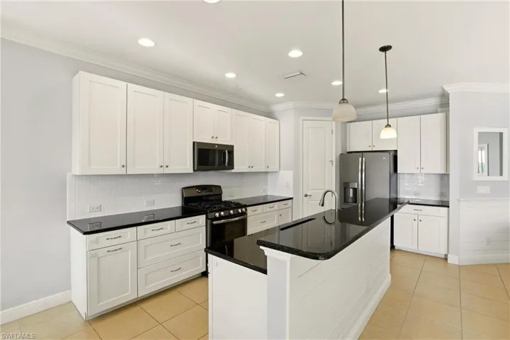 Kitchen featuring white cabinetry, pendant lighting, stainless steel appliances, light tile patterned flooring, and ornamental molding