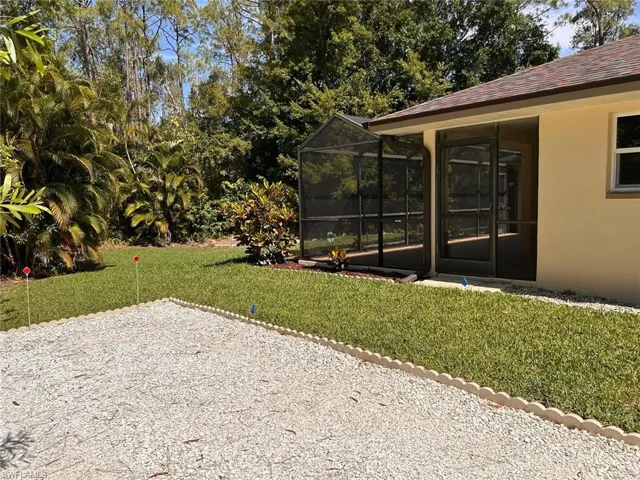 View of grassy yard with glass enclosure, a sunroom, and view of wooded area