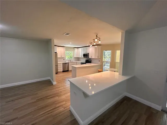Kitchen with a peninsula, white cabinetry, light wood-style floors, decorative backsplash, and appliances with stainless steel finishes