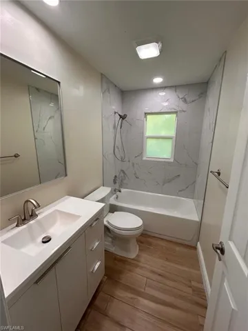 Bathroom with vanity, light wood-type flooring, and a combined bath / shower with marble appearance