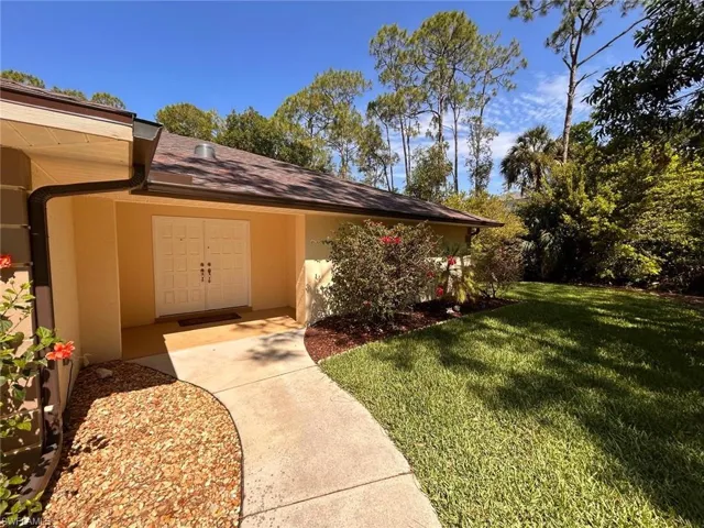 View of exterior entry featuring stucco siding, a yard, and roof with shingles