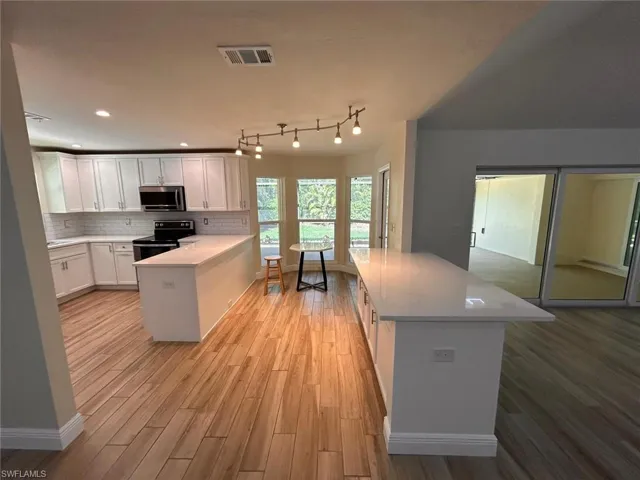 Kitchen featuring a peninsula, white cabinets, backsplash, electric range oven, and light wood-style floors