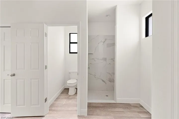 Bathroom with wood-type flooring, toilet, and a tile shower