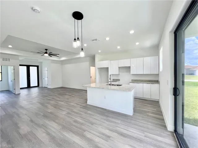 Kitchen with white cabinets, a center island with sink, light hardwood / wood-style flooring, pendant lighting, and sink