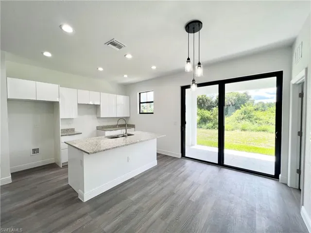Kitchen with sink, decorative light fixtures, white cabinets, light stone counters, and a kitchen island with sink