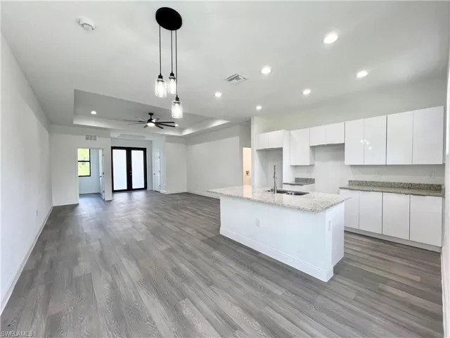 Kitchen with light hardwood / wood-style flooring, white cabinets, a center island with sink, and ceiling fan