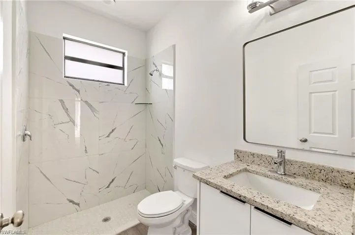Bathroom featuring toilet, vanity, and a tile shower