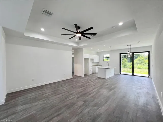 Unfurnished living room featuring dark wood-type flooring, ceiling fan, a raised ceiling, and sink