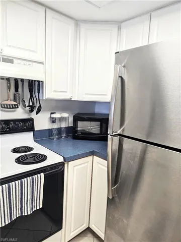 Kitchen featuring white cabinets, white electric stove, stainless steel fridge, and custom range hood