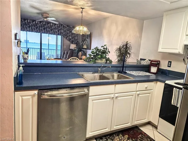 Kitchen featuring sink, light tile patterned floors, dishwasher, ceiling fan, and white cabinets