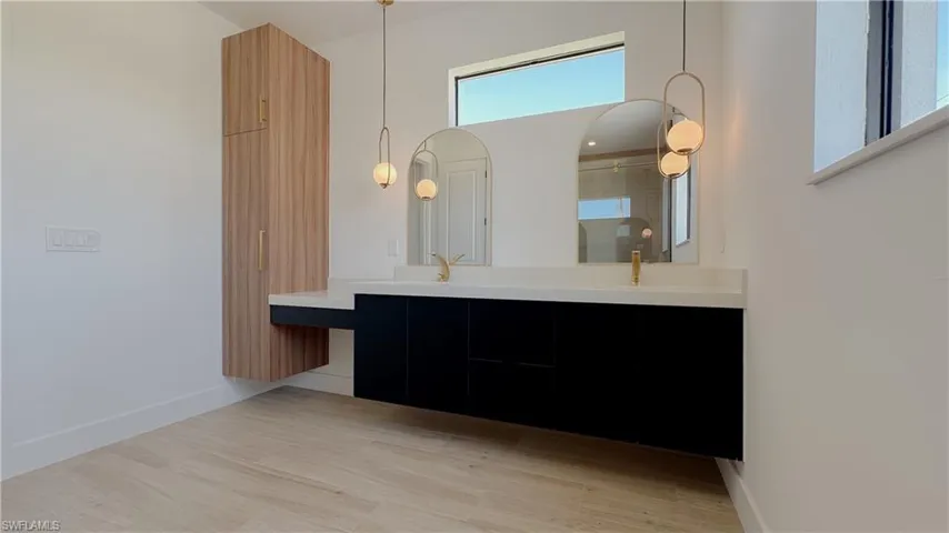Full bath featuring double vanity, wood finished floors, baseboards, and a sink