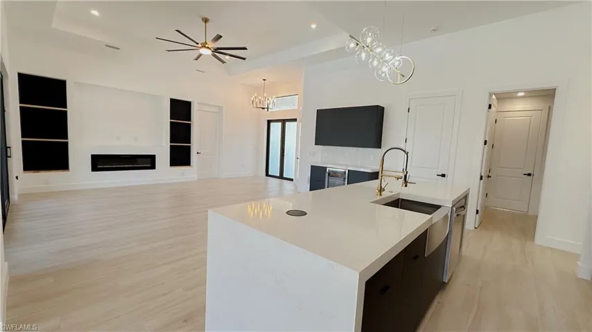 Kitchen with a glass covered fireplace, light countertops, an island with sink, and light wood finished floors