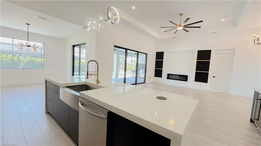 Kitchen featuring open floor plan, a center island with sink, dishwasher, light countertops, and a sink