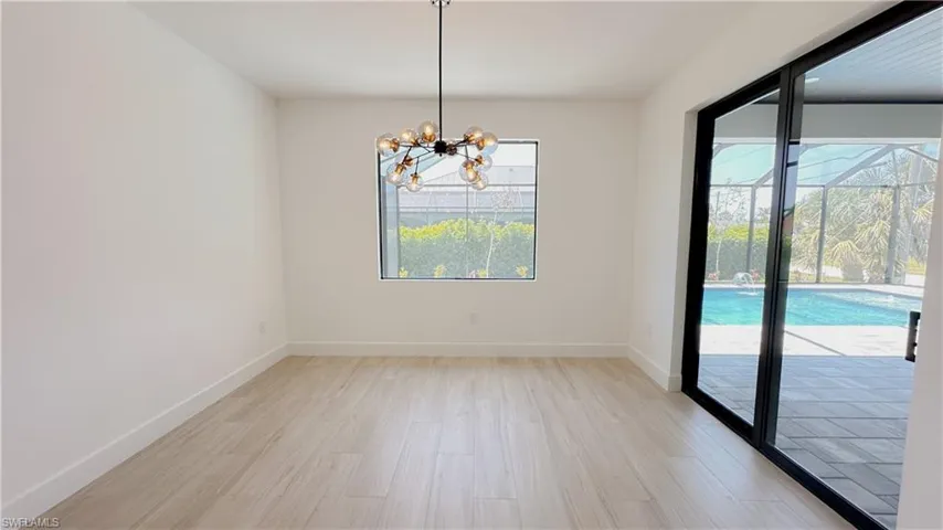 Spare room with baseboards, a notable chandelier, and light wood finished floors