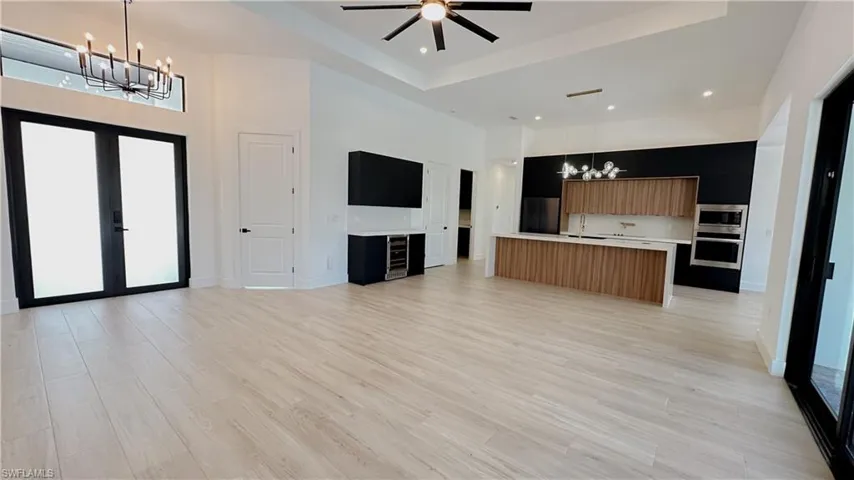 Unfurnished living room featuring light wood-style flooring, baseboards, a towering ceiling, and ceiling fan with notable chandelier