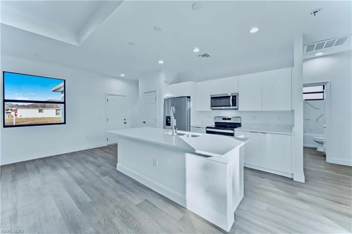 Kitchen featuring a center island with sink, white cabinets, stainless steel appliances, and light hardwood / wood-style floors