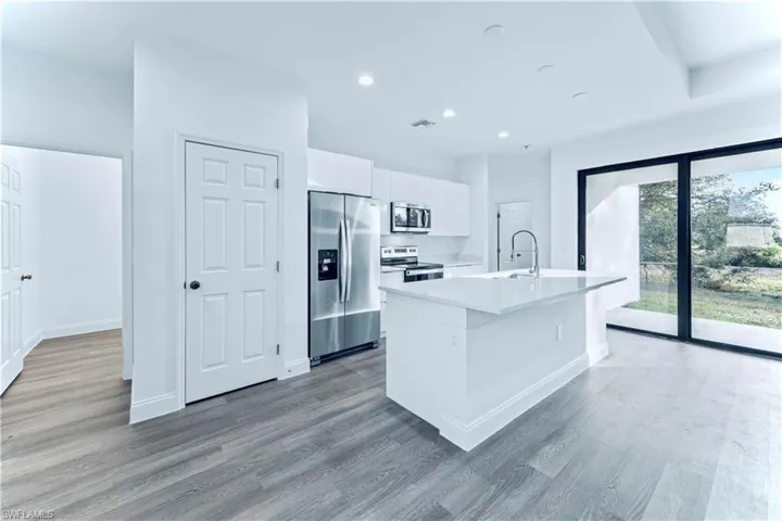 Kitchen featuring hardwood / wood-style floors, a center island with sink, white cabinets, sink, and appliances with stainless steel finishes