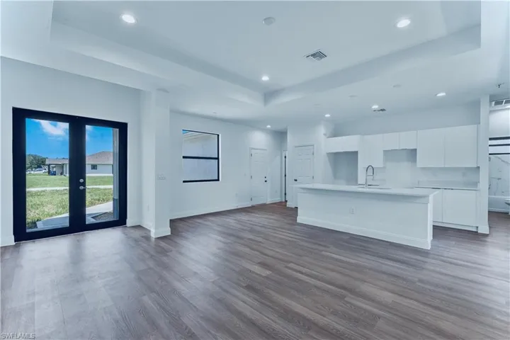 Kitchen with white cabinets, french doors, a center island with sink, and a tray ceiling