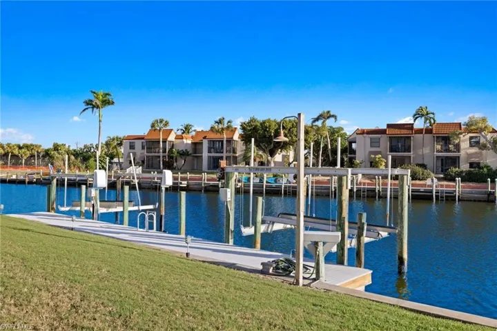 Dock with boat lift, a water view, and a lawn