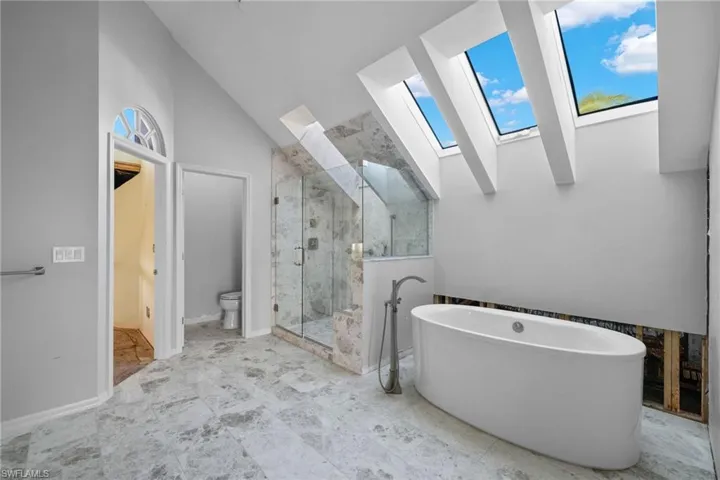Primary Bathroom featuring a skylight, a marble finish shower, lofted ceiling, and a freestanding tub