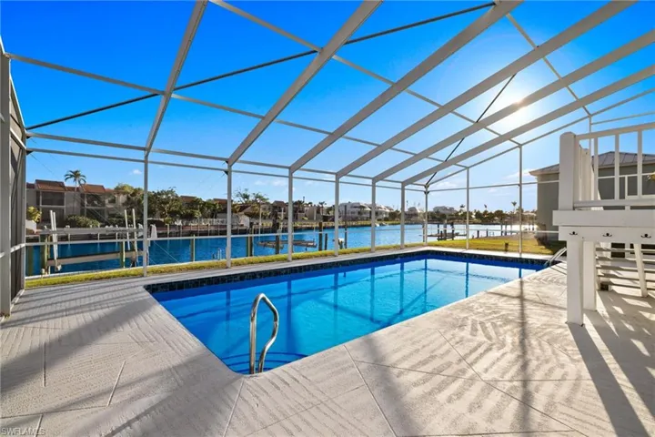 Outdoor pool featuring a sunroom, a patio area, a water view, glass enclosure, and a dock