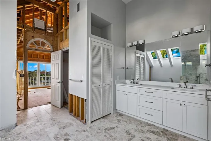 Primary Bathroom featuring a closet, double vanity, a high ceiling, and a marble finish shower