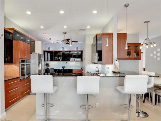 Kitchen featuring backsplash, hanging light fixtures, appliances with stainless steel finishes, a kitchen bar, and kitchen peninsula